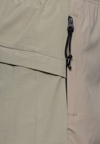 Lätta, beige utomhusbyxor med ett texturerat, rutigt mönster. Har en sidodragkedjeficka och justerbar dragsko i midjan.