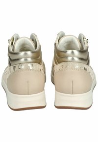 Beige tenisky s metalickým zlatým kotníkem, texturovanými akcenty a bílou podrážkou. Mají dekorativní výřezy blízko paty a hladký povrch.