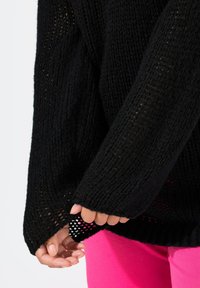 Maglione nero lavorato a maglia con un design rilassato e testurizzato e una tessitura aperta. Il polsino presenta un orlo a strati, rivelando uno strato di rosa sottostante.