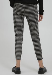 Zwart-wit geblokte broeken met een slim fit, cropped lengte en lichte fraying aan de onderkant, gedragen met zwarte instap schoenen.