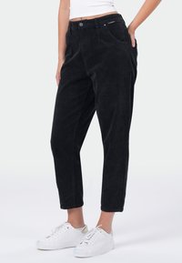 Zwarte corduroybroek met een hoge taille, taps toelopende benen en zijzakken, gecombineerd met witte sneakers. Textiel met een gestructureerde stof en subtiele ribbels.