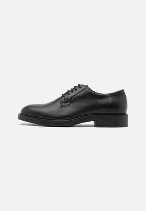 Zapato Oxford de cuero negro con cordones, punta redondeada y tacón bajo apilado, mostrado de perfil sobre un fondo claro.