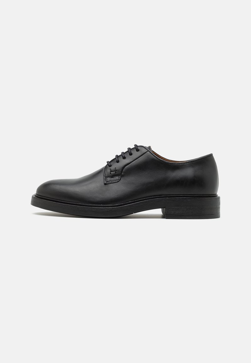 Chaussure Oxford noire en cuir à lacets, avec bout arrondi et petit talon empilé, vue de profil sur un fond clair.