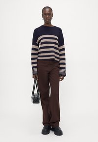 Marineblå og beige stripete strikkegenser, kort design, kombinert med brune vide bukser og en liten svart veske. Sorte kraftige sko fullfører antrekket.