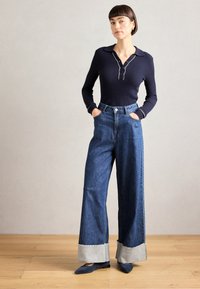 Polo shirt a maniche lunghe rigato blu navy con colletto, abbinato a jeans blu a vita alta con gamba ampia e orlo sfrangiato con dettagli in denim chiaro.