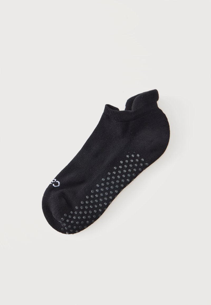 Chaussette noire à la cheville avec des picots antidérapants en caoutchouc sur la semelle, présentée sur un fond blanc uni.