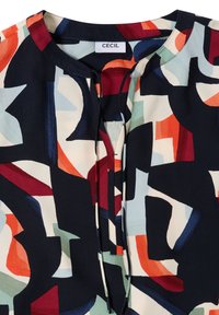 Blouse à motifs abstraits multicolores avec encolure ronde, fente centrale devant et deux fines cordelettes au col.