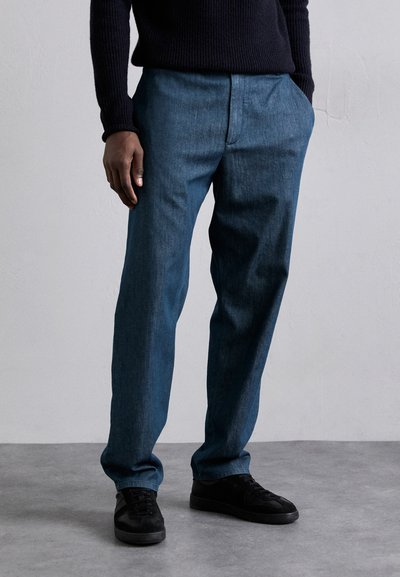 Lässige, dunkelblaue Denim-Hosen mit glatter Textur, Seitentaschen und flachem Bund. Kombiniert mit schwarzen Turnschuhen.