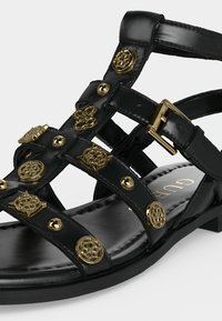 Μαύρο δερμάτινο σανδάλι με πολλαπλά λουριά διακοσμημένα με χρυσά ανθικά καρφιά και χρυσή αγκράφα στο λουράκι του αστραγάλου.