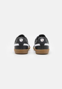Sneaker nere in pelle con strisce bianche, suola in gomma, e logo prominente sul tallone; presenta un colletto imbottito e una superficie liscia.