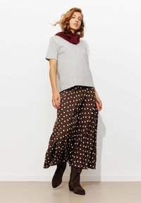 T-shirt gris à manches courtes associé à une jupe midi à pois marron et des bottines à talons marron. La jupe a un design fluide et une texture douce.