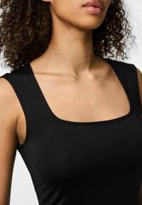 Top nero a canotta con scollatura quadrata. Realizzato in tessuto liscio ed elasticizzato, presenta spalline larghe e una silhouette aderente.