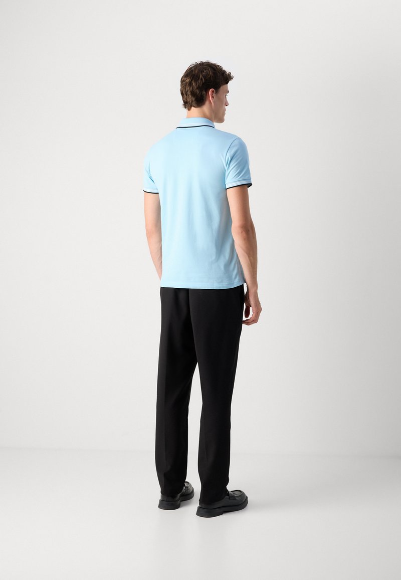 Polo bleu clair avec des bordures noires, assorti à un pantalon noir et des chaussures noires. Tissu lisse avec un design de col classique.