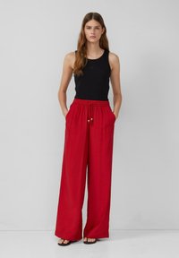 Débardeur noir à côtes, pantalon en lin rouge ample avec poches, taille élastique et cordon décoratif avec perles.