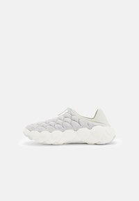 Világosszürke sneaker, steppelt felsőrésszel, elasztikus gallérral és vastag fehér talppal. Kerek díszítések és minimális dizájn elemek jellemzik.