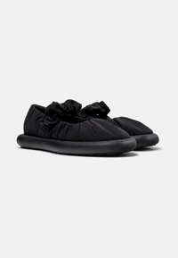 Scarpe nere slip-on con tomaia in tessuto arricciato e suola in gomma morbida. Presentano una finitura texture e un design a punta arrotondata.