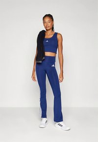 Námořnicky modrý sportovní komplet se střiženým tílkem a kalhotami s vysokým pasem s bílými pruhy na bocích. Nosit s černým ručníkem přehozeným přes rameno.