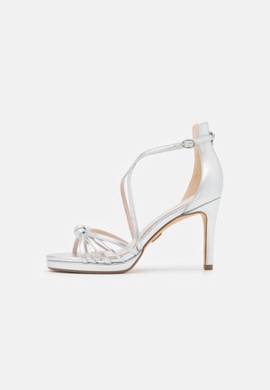 Silver strappy high-heel sandal with an open toe, knot detail, and ankle strap. Smooth, shiny material with a light, cushioned sole.