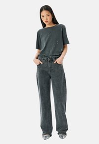Camiseta gris de manga corta con tachuelas decorativas, combinada con unos vaqueros gris de pierna ancha con un patrón texturizado y un cinturón clásico.