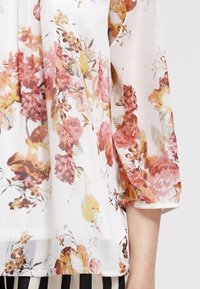 Blusa leggera e trasparente con motivo floreale nelle tonalità di rosa, giallo e arancione; presenta maniche a tre quarti e un orlo dritto.