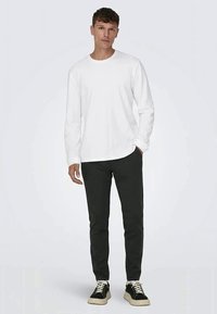 Long-sleeve white cotton t-shirt with a crew neck, paired with dark grey pants and black sneakers with white soles and laces.