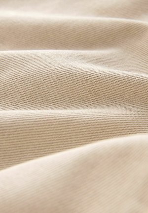 Hellbeiges Stoffmaterial mit einer weichen, strukturierten Oberfläche. Das Material zeigt ein dezentes diagonales Webmuster mit sanften Falten und Knicken.