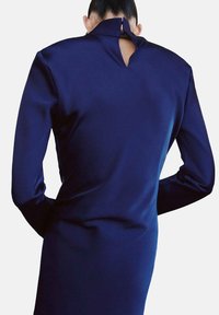 Robe à manches longues bleu marine avec un col montant et une ouverture en forme de goutte dans le dos, confectionnée dans un tissu lisse et texturé.