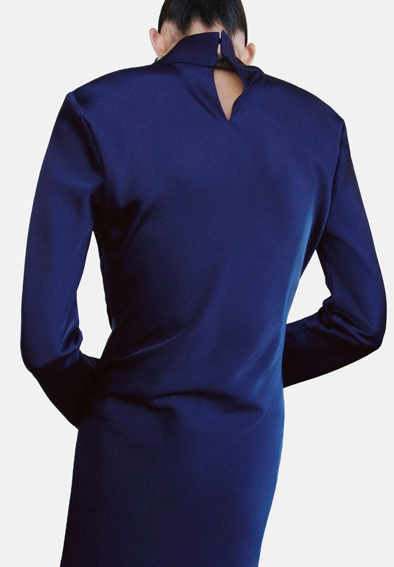 Robe à manches longues bleu marine avec un col montant et une ouverture en forme de goutte dans le dos, confectionnée dans un tissu lisse et texturé.