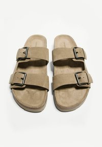 Beige velúr szandálok két állítható pánttal és fém csattal. Lapos talp, amelynek texturált felülete van a tapadás érdekében. Egyszerű, funkcionális dizájn.