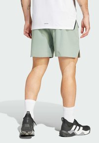 Men's light green shorts made of textured fabric, complemented by black athletic shoes and white socks. Features split side seams.
