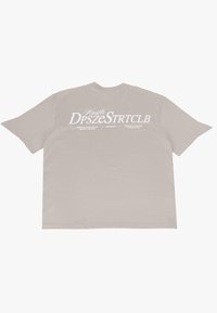Overdimensioneret beige t-shirt lavet af bomuld. Har stor hvid tekst, der siger "Hustle DpszeStrtclb" samt yderligere detaljer på bagsiden.
