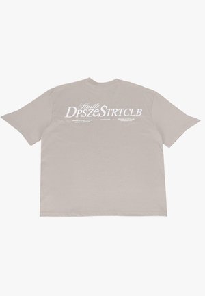 Overdimensioneret beige t-shirt lavet af bomuld. Har stor hvid tekst, der siger "Hustle DpszeStrtclb" samt yderligere detaljer på bagsiden.