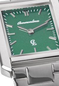 Τετράγωνο ασημένιο ρολόι χειρός με πράσινο καντράν, ασημένιους δείκτες ώρας και δείκτες, δείχνοντας 10:10, σε μεταλλικό βραχιόλι με κρίκους.