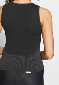 Svart atletisk linne med ribbad textur, med en figursydd design och kontrasterande stickad panel vid midjan. Enkelt logotyp vid fållen.