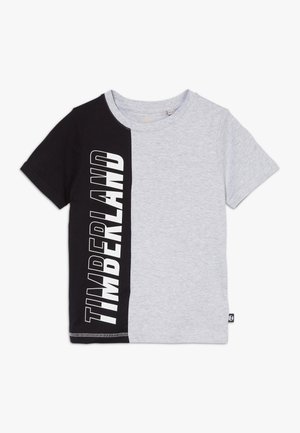 Koszulka z krótkim rękawem, podzielona pionowo na czarną i jasnoszarą, z dużym białym logo Timberland na czarnej połowie.