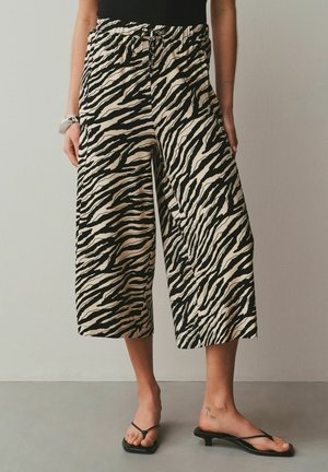 Woman wearing beige and black zebra-striped wide-leg cropped pants, black sleeveless top, and black heeled sandals.