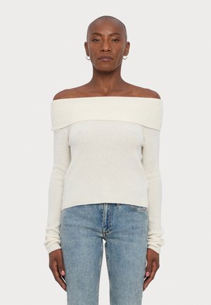 Pull crème à épaules dénudées avec texture côtelée, manches longues et coupe ajustée, associé à un jean droit bleu clair.
