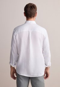 Camicia bianca in lino a maniche lunghe con colletto a punta e maniche arrotolate, dotata di una cucitura sul retro e orlo curvo. Vestibilità standard.