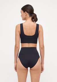 Black sports bra with a scooped back and thick straps paired with high-waisted swim bottoms, featuring a smooth, stretchy fabric.