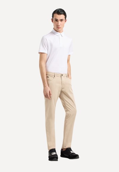 Polo blanc à manches courtes, chinos beiges et baskets noires. L'ensemble présente un col classique et des poches frontales standard.