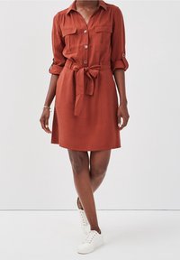 Robe couleur rouille en tissu léger, dotée d'une fermeture boutonnée à l'avant, de deux poches poitrine et d'une ceinture à nouer à la taille.