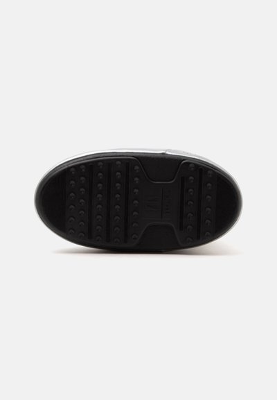 Semelle de basket noir et blanc montrant une semelle texturée avec de petites crampons arrondis et une zone centrale avec logo en relief.