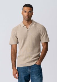 Beige kortærmet polo skjorte med ribbet tekstur og V-udskæring. Sammen med blå denim jeans, som viser en afslappet pasform.