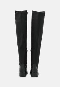 Botas negras hasta la rodilla hechas de un textil suave con un acabado liso, con cremalleras laterales y un tacón grueso negro.
