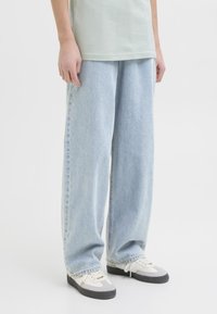 Ljusblå, vida jeans i denimtyg med fransade kanter, med en avslappnad passform och subtil blekning, tillsammans med grå och vita sneakers.