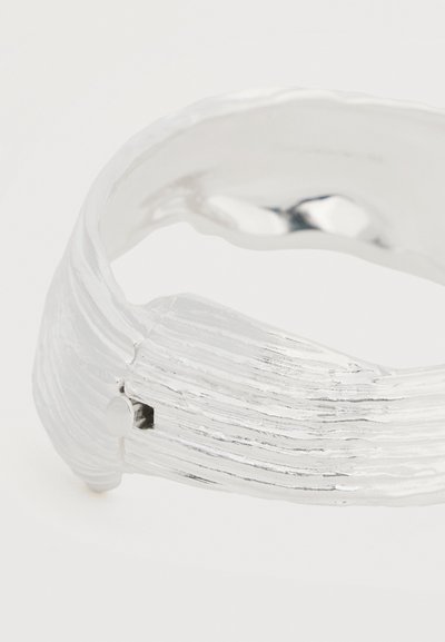 Ασημένιο υφασμένο ανοιχτό δαχτυλίδι με οριζόντιες αυλακώσεις και μια μικρή στρογγυλή καρφίτσα στη μία πλευρά.