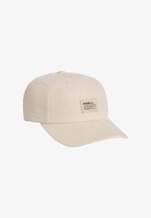 Beige cotton baseball cap with sewn rectangular patch reading "REELL" and text on front panel, curved brim, and ventilation holes on top.