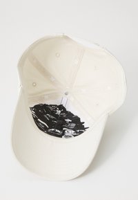 White baseball cap featuring a smooth fabric with an inner lining displaying a black and white graphic pattern of stacked objects.