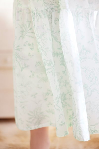 Vestido floral de tom verde claro feito de tecido transparente, apresentando cintura franzida e mangas longas e fluidas. Textura suave e cor suave.