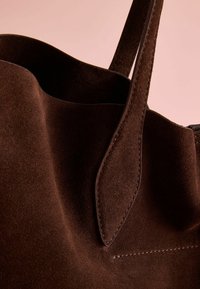 Brown suede tote bag with smooth texture, featuring a single strap and visible stitching details along the edges.